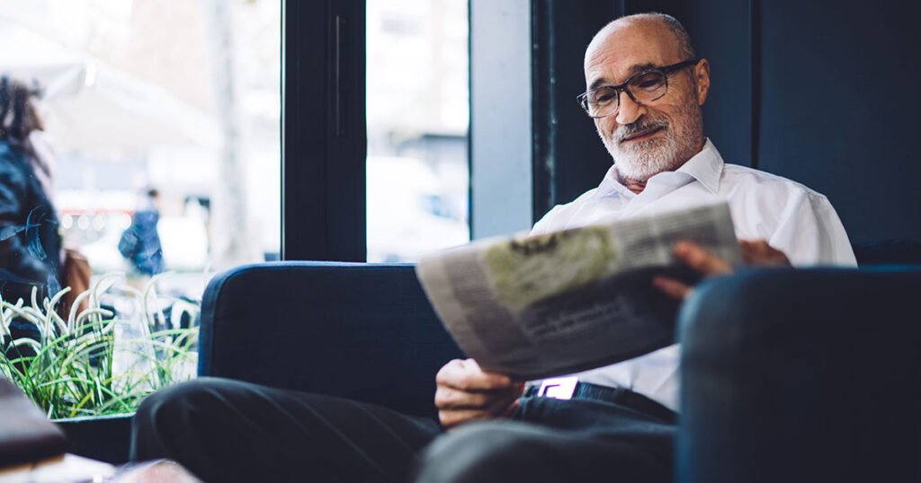 Retired American expat relaxing in a café abroad while reading a newspaper