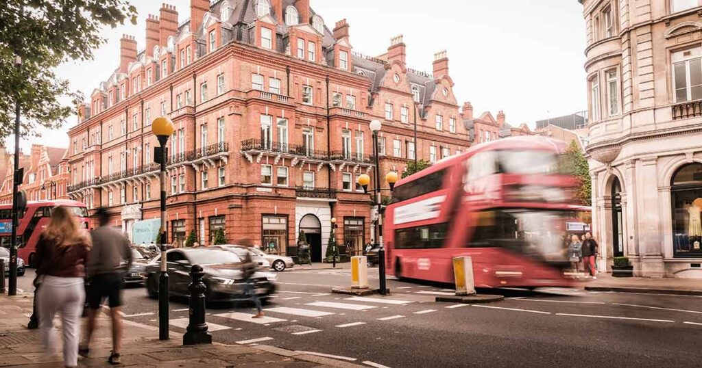 Luxury London street scene with red brick townhouses, double‑decker bus and pedestrians illustrating UHNW family neighborhoods and cross‑border wealth management in the UK.