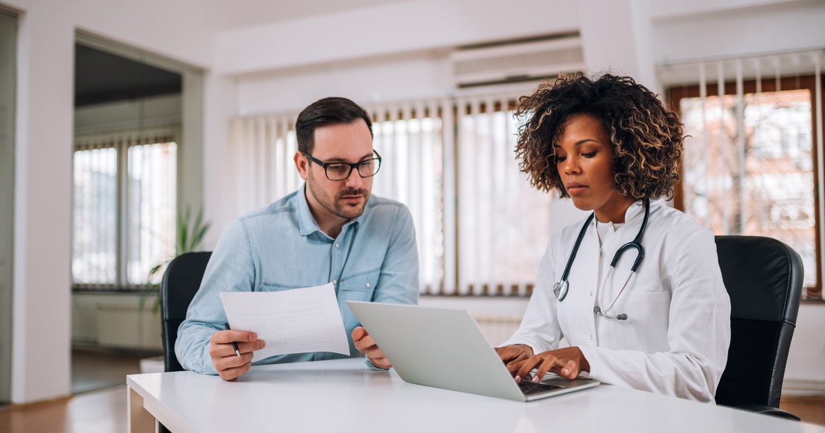 Physician reviewing financial documents with an advisor while working on a laptop