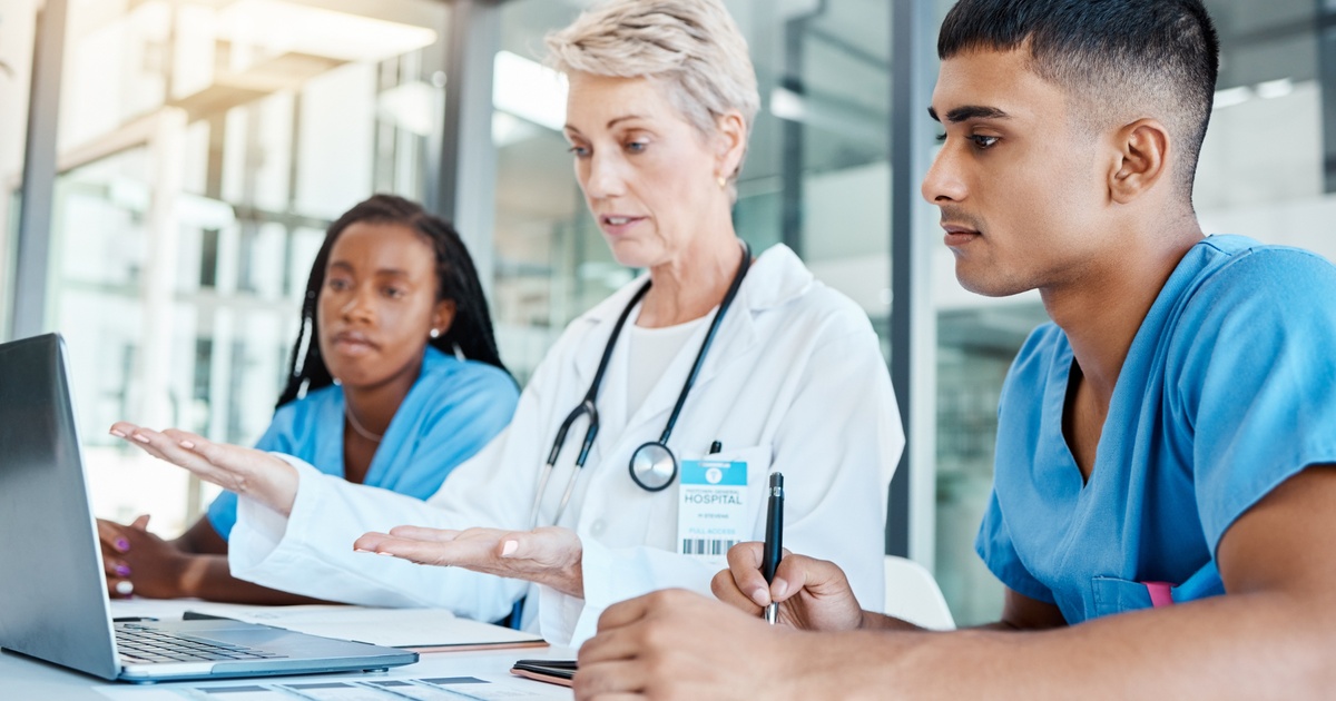 Medical professional leading a discussion with clinicians around a laptop