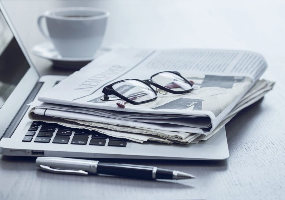Newspaper with reading glasses sitting on top of laptop