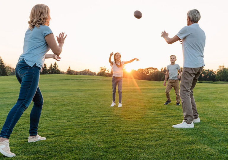 Multigenerational family playing football together on a lawn at sunset, representing the lasting family wealth and shared values that family office investment services are designed to preserve and grow