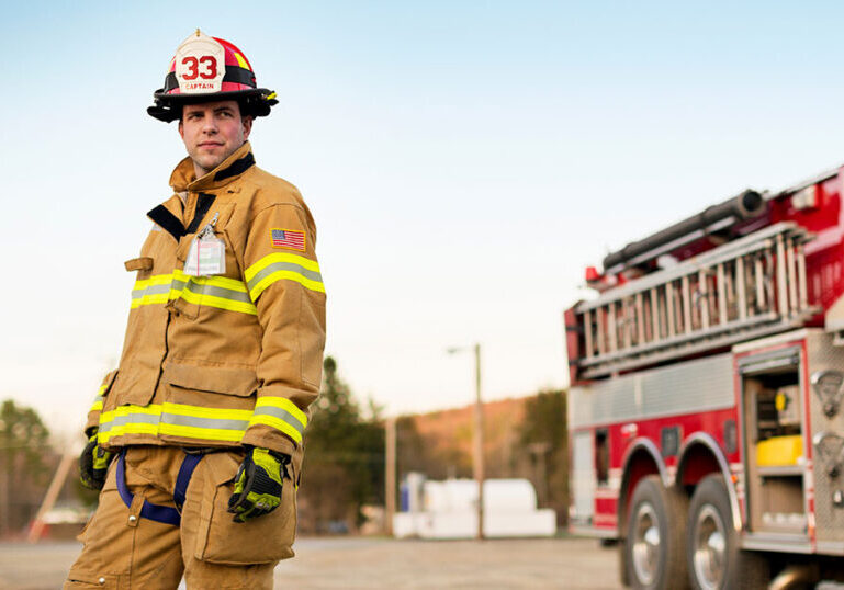 Firefighter captain standing in full gear in front of a fire truck, representing public safety employees who rely on a governmental 457b deferred compensation plan to bridge retirement income