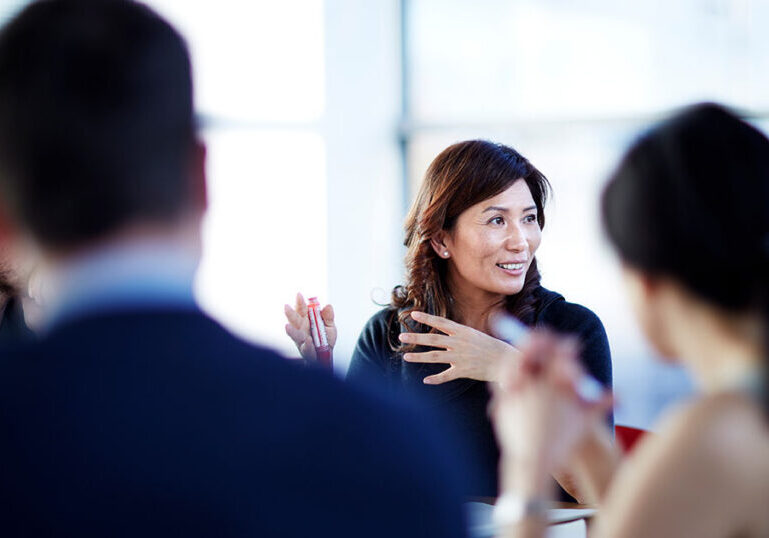 Professional woman leading a discussion with colleagues at a bright conference table, representing the collaborative guidance available to beginners starting their retirement planning journey