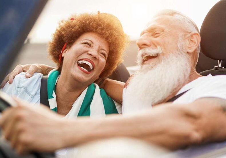 Trendy senior couple having fun inside convertible car - Multiracial mature people on a road trip in summer vacation with cabriolet car