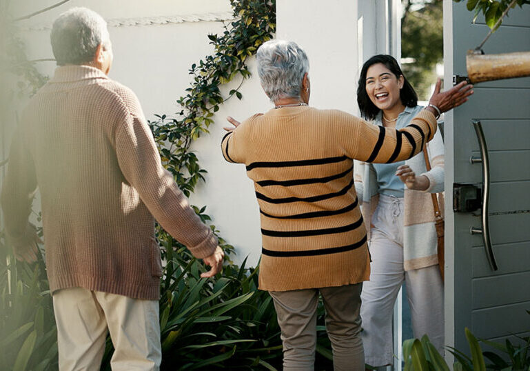 Older parents warmly greeting their adult daughter at the front door, symbolizing family support and the importance of setting healthy boundaries when financially helping grown children.